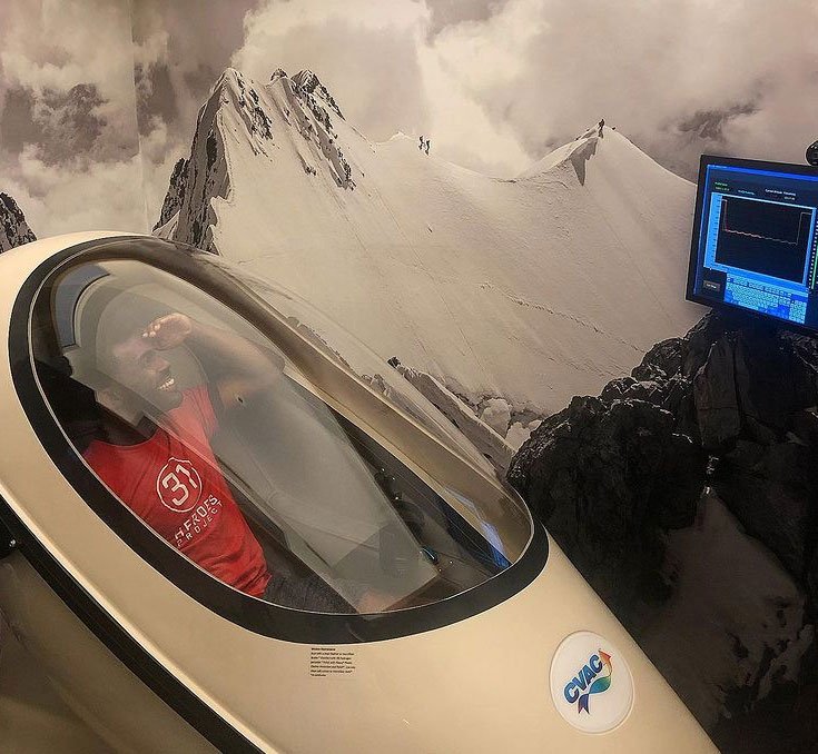 An athlete lying back inside a closed CVAC Pod beside the session control screen.