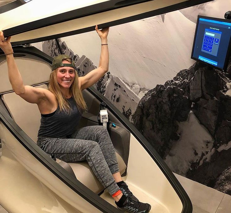 An athlete seated inside an open CVAC Pod, holding the raised canopy, at a recovery studio in New York.