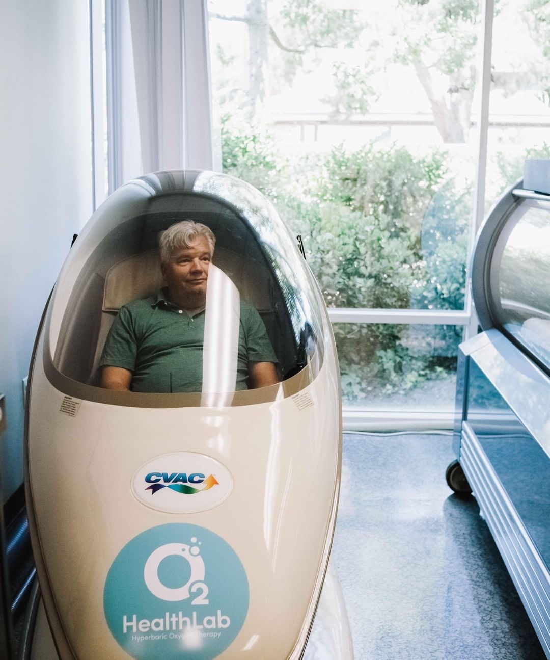 A CVAC Pod at O2 HealthLab, its clear canopy lowered over a seated occupant, with the CVAC mark on the shell.